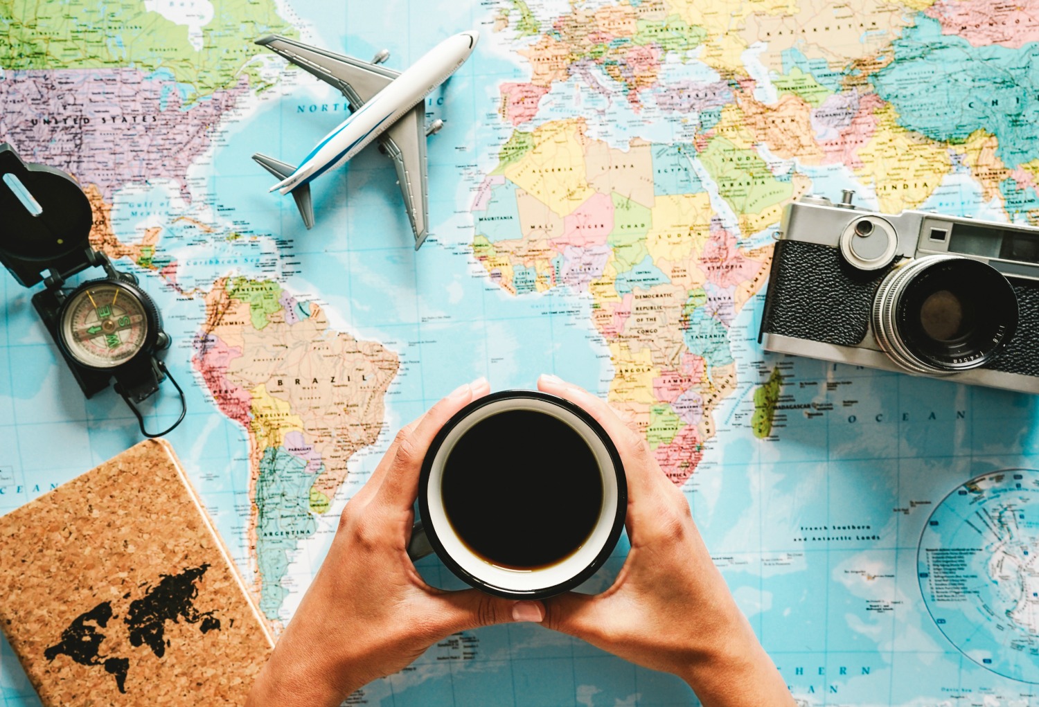 Top view of young woman planning her vacation using world map while drinking coffee - Tourist pointing the next travel destination - Concept of adventure, tourism, and traveling people lifestyle