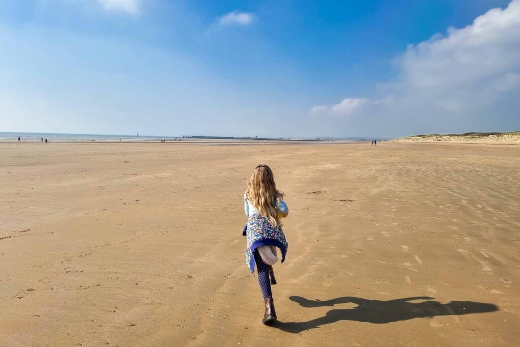 Girl running along an open sandy beach in Camber Sands, Sussex, UK